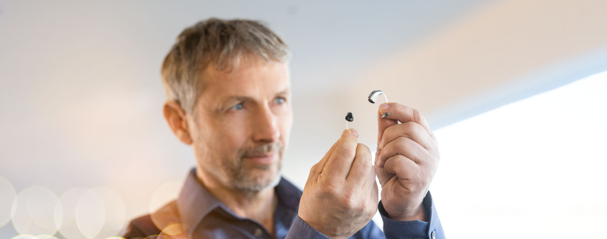 Vergleich von Im Ohr Hörgerät und Hinter dem Ohr Hörgerät. Mann hält die Hörgeräte in der Hand