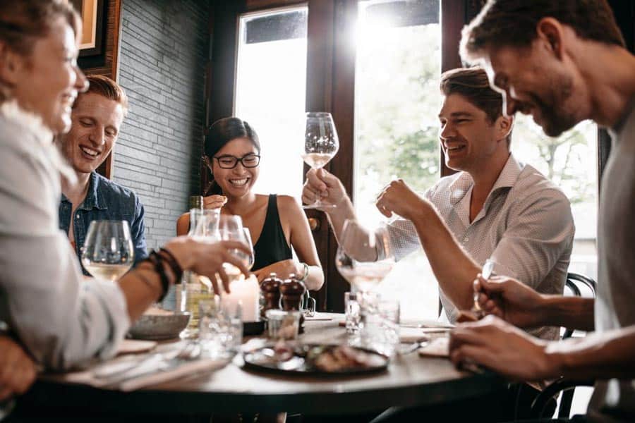 Eine Gruppe von Freunden im Restaurant. Sie lachen. Ein junger Mann möchte mit einem Glas Wein anstoßen